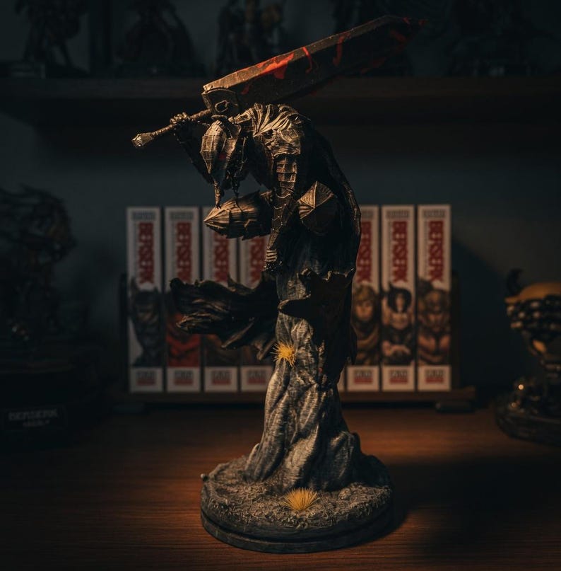 Puede incluir: Una figura detallada de un guerrero con armadura oscura y texturizada, agachado sobre una base rocosa con peque&ntilde;os mechones de hierba amarilla. El personaje sostiene una espada masiva y desgastada sobre sus hombros, con tonos met&aacute;licos.