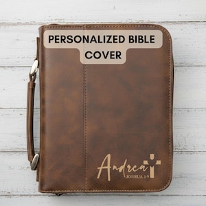May include: Brown leather Bible cover with the text "PERSONALIZED BIBLE COVER" at the top. The cover has a handle and a zipper closure. The name "Andrea" and a cross are printed on the front, with the text "Joshua 1:9" below.