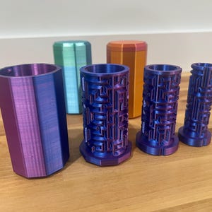 May include: Five 3D printed containers, two are purple and blue, two are purple and blue with a textured pattern, and one is orange. The containers are on a wooden surface.