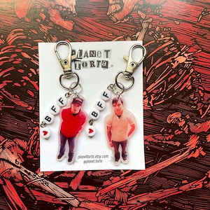 May include: Two keychains featuring cutouts of people attached to silver lobster clasps. Each keychain has white beads spelling BFF and a small red heart bead. The display card features the text PLANET TORTA, planettorta.etsy.com, and planet.torta.