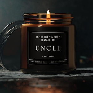 May include: A lit candle in a brown glass jar with a black lid. The label reads "SMELLS LIKE SOMEONE'S GONNA BE AN UNCLE EST. 2020." The candle is on a dark surface with a dark background. The candle is likely scented.