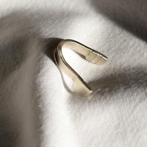 May include: A silver-colored, curved metal object, possibly a jewelry clasp or finding, rests on a white, textured fabric. The object has a smooth, reflective surface and a simple, minimalist design. The lighting creates shadows that highlight its shape.
