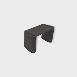 May include: A dark gray, U-shaped bracket with a flat top and two oblong holes. The bracket has rounded sides and appears to be made of a solid, possibly plastic, material. The object is set against a plain, light background.