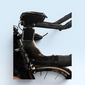May include: Close-up of a black road bicycle with a sleek design. The handlebars are wrapped in black tape, and a small black bag is mounted on the frame. The wheel has the word "Dura-" visible on the rim.