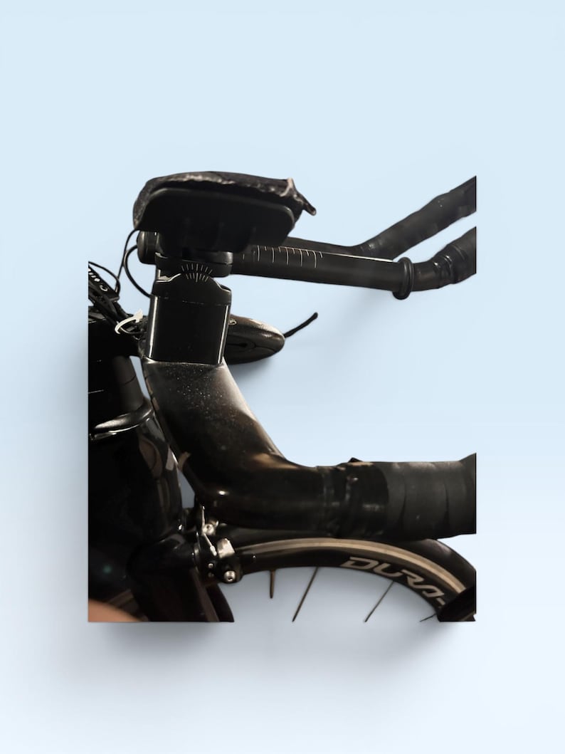 May include: Close-up of a black road bicycle with a sleek design. The handlebars are wrapped in black tape, and a small black bag is mounted on the frame. The wheel has the word "Dura-" visible on the rim.