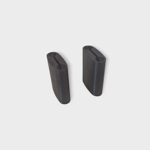 May include: Two black, rectangular objects with rounded edges and a central groove. The objects are identical in shape and size, and appear to be made of a solid material. They are positioned against a plain, light background.