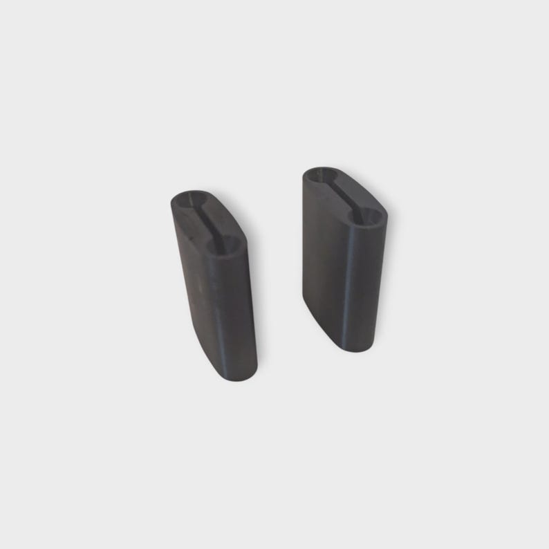 May include: Two black, rectangular objects with rounded edges and a central groove. The objects are identical in shape and size, and appear to be made of a solid material. They are positioned against a plain, light background.