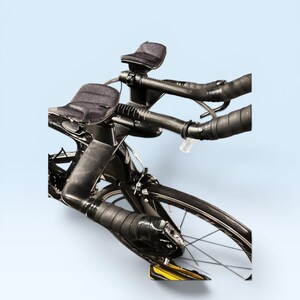 May include: A black road bicycle with aero bars and black handlebar tape. The bike has a sleek design with a black frame, black wheels, and a light blue background. The bike is designed for speed and efficiency.