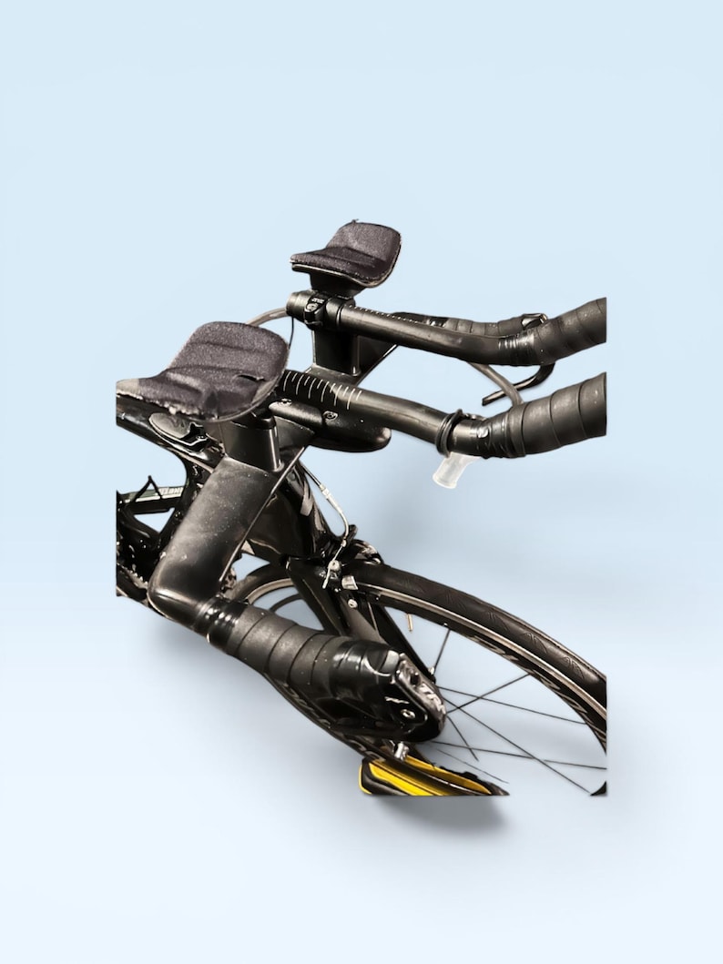 May include: A black road bicycle with aero bars and black handlebar tape. The bike has a sleek design with a black frame, black wheels, and a light blue background. The bike is designed for speed and efficiency.