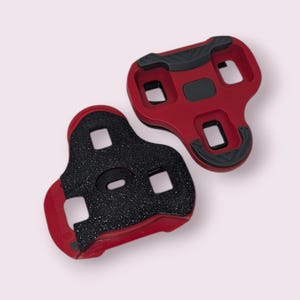 Peut inclure: Deux cales de vélo rouges et noires. Les cales ont une forme rectangulaire avec trois trous carrés et une surface noire texturée pour l'adhérence. Les cales sont conçues pour se fixer aux pédales de vélo.