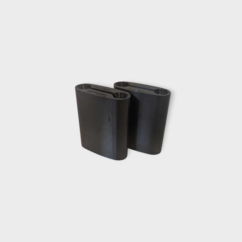 May include: Two black, rectangular knife holders with an oval top and a slot for the knives. The holders are made of a solid, matte material and are positioned side by side against a white background. The holders are designed to store knives.