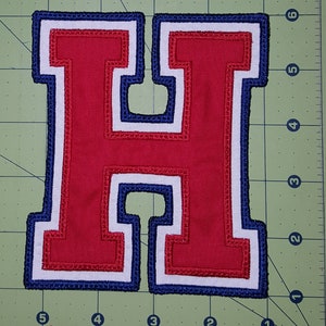 May include: Red felt letter H with white and blue trim. The letter is stitched with a zig-zag pattern around the edges.