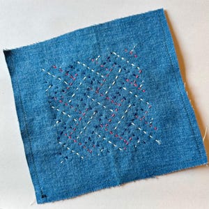 May include: A blue denim square with white, pink, and blue embroidery in a geometric pattern.