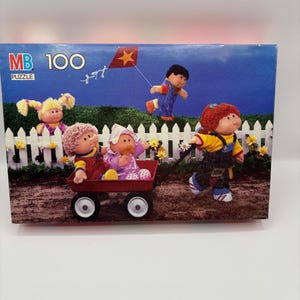 May include: A vintage MB 100-piece puzzle box featuring Cabbage Patch Kids. The box art depicts the dolls playing with a red wagon, a kite, and a white picket fence against a blue sky. A nostalgic toy.