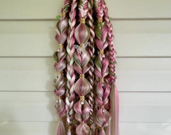 Op de afbeelding: Een set synthetische hairextensions met meerdere vlechten in tinten roze, wit en olijfgroen. Het haar is versierd met goudkleurige metalen manchetjes, kleine witte kraaltjes en een doorzichtig vlindervormig haaraccessoire.