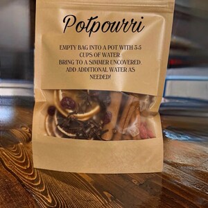 May include: A brown paper bag labeled "Potpourri" with instructions. The bag contains dried orange slices, cinnamon sticks, and other aromatic ingredients. The text on the bag reads: "EMPTY BAG INTO A POT WITH 3-5 CUPS OF WATER. BRING TO A SIMMER UNCOVERED. ADD ADDITIONAL WATER AS NEEDED!"