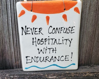 Never confuse hospitality with endurance ceramic hanging sign