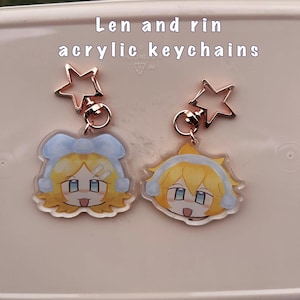 May include: Two acrylic keychains featuring anime characters Len and Rin. The keychains are attached to gold star-shaped charms.