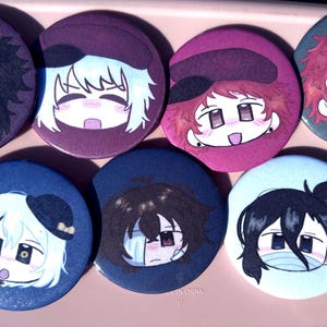 Puede incluir: Colección de ocho botones redondos con ilustraciones de personajes de estilo anime. Cada botón presenta un diseño de personaje diferente con varios colores de pelo, sombreros y expresiones. Los botones están sobre una superficie rosa.