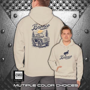 May include: Beige hoodie with a front pocket and a hood. The back of the hoodie features a blue and white graphic of a Bronco SUV with the word "Bronco" above it. The front of the hoodie has a Bronco logo. The text "MULTIPLE COLOR CHOICES" is at the bottom.
