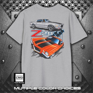 May include: A gray t-shirt featuring illustrations of two classic Z28 Camaro cars, one silver and one orange with black stripes. The design includes the text "Z28" and palm trees. The bottom of the shirt reads "MULTIPLE COLOR CHOICES".
