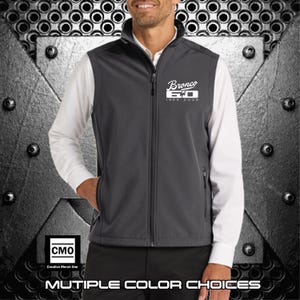 May include: A charcoal gray vest with a full zipper, featuring the text "Bronco 50 1966-2023" in white. The vest is worn over a white long-sleeve shirt. The image also includes the text "MULTIPLE COLOR CHOICES".
