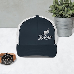 Op de afbeelding: Een marineblauwe en witte truckerpet met het woord "Bronco" in witte letters geborduurd. De pet heeft een witte mesh achterkant en een gebogen klep. Een witte paardenafbeelding staat boven het woord "Bronco".