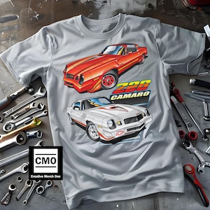 May include: Gray t-shirt with a graphic of two red and white 1978 Chevrolet Camaro Z28 cars. The text "Z28 CAMARO" is printed on the shirt. The shirt has a small logo in the lower left corner that says "CMO Creative Merch One".