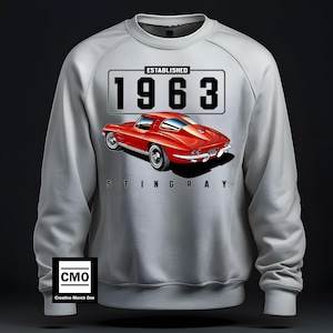 May include: A grey sweatshirt featuring a red 1963 Corvette Stingray printed on the front. The car has a black number plate that reads "ESTABLISHED 1963".