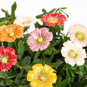 Puede incluir: Un ramo de flores de cerámica en varios colores, incluyendo rosa, rojo, naranja, amarillo y blanco. Las flores están dispuestas en una base verde de hojas, creando una exhibición floral realista y vibrante.