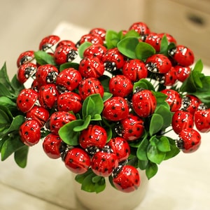 May include: A bouquet of artificial flowers with red ladybug-shaped ornaments and green leaves.
