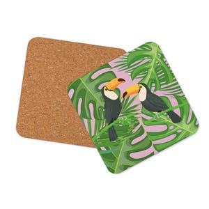 May include: Two square coasters. One is cork, the other features a toucan design. The toucans have black bodies and yellow beaks, set against a backdrop of green leaves and a pink background. The birds are perched on a green vine.
