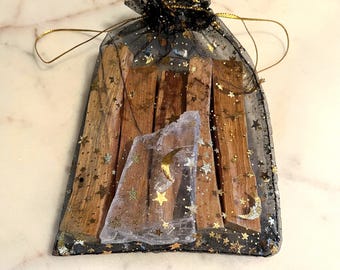 May include: A black mesh bag with gold stars and moons contains wooden sticks. A smaller, sheer white bag with gold stars, moons, and a crescent moon is inside. The bag is tied with a gold drawstring.