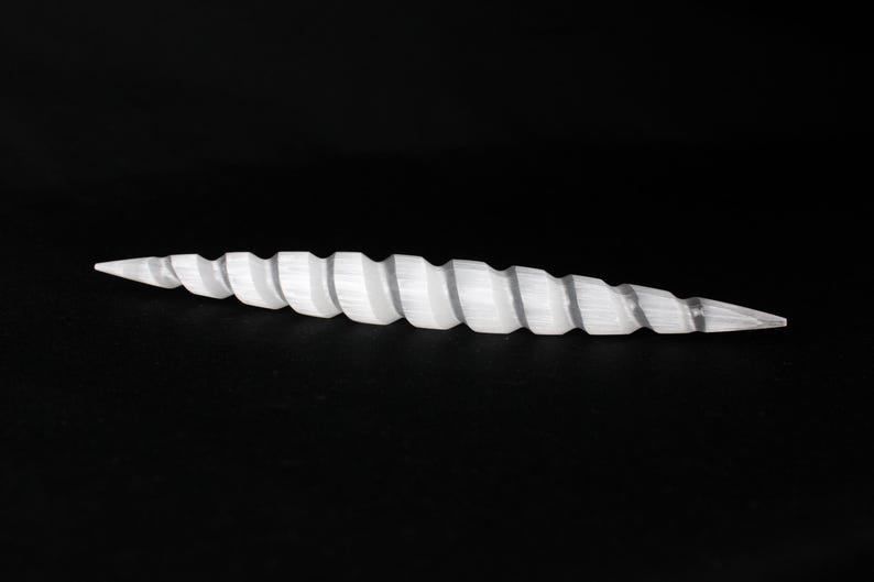 May include: A white, spiraled, horn-shaped object against a black background. The object has a pointed tip on both ends and a series of ridges along its length. The overall shape is elongated and symmetrical.