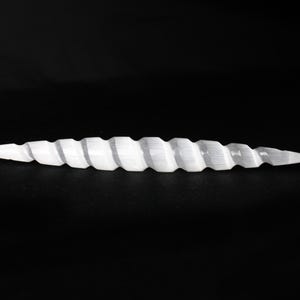 May include: A white, spiraled, selenite crystal wand. The wand has a pointed tip on both ends and a ridged, twisted design along its length. The background is solid black.