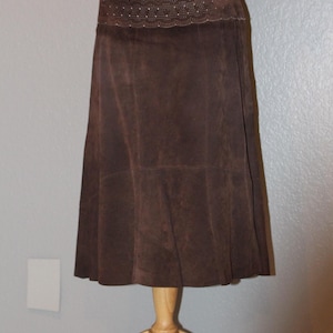 May include: A brown suede skirt with a decorative lace waistband. The skirt is knee-length and has a flared silhouette.