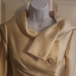 Puede incluir: Una chaqueta de color crema con un cuello grande y doblado y un cierre de botón único.