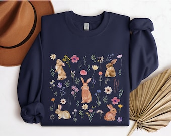 Può includere: Felpa blu navy con stampa floreale con conigli marroni. I conigli sono circondati da fiori in tonalità rosa, viola, giallo e blu.