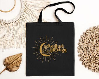 May include: Black canvas tote bag with gold text that reads "adventure life yoga" and a gold graphic of a crescent moon with a flower inside.