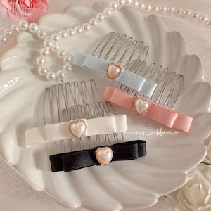 May include: Four hair combs with pearl heart embellishments and ribbon bows in white, pink, blue, and black.