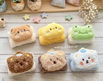 Puede incluir: Seis muñequeras de felpa con caras de animales bordadas, incluyendo un oso marrón, un pollito amarillo, una rana verde, un oso marrón oscuro, un oso beige y un oso blanco con un gorro de fiesta azul, con texturas suaves y el texto merry_ribbon.co.
