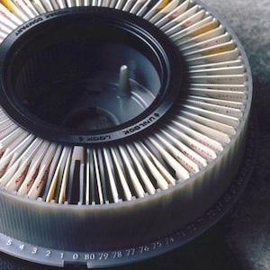 May include: A gray plastic slide projector carousel with a black rim and a clear center. The carousel is filled with 80 slides, each with a white card and red text. The text on the slides reads "Kodak" and "OCT. 1980". The carousel has a number scale from 1 to 80.