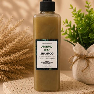 May include: A clear, rectangular shampoo bottle with a black pump dispenser. The bottle contains a light green liquid and has a label that reads "AMBUNU LEAF SHAMPOO." The bottle is on a textured, beige surface. The net weight is 16 oz (454 g).