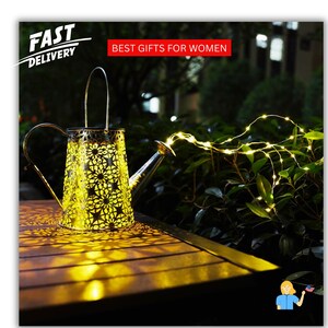 May include: A decorative, gold-colored watering can-shaped lantern with a floral pattern, illuminated from within. The lantern is on a wooden surface, with string lights extending from the spout. Text reads "FAST DELIVERY" and "BEST GIFTS FOR WOMEN".