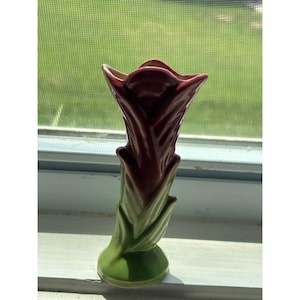 Peut inclure: Un vase en céramique en forme de fleur de tulipe avec une partie supérieure rouge bordeaux profond et une base vert clair présentant des détails de feuilles sculptées. Le vase a une finition lisse et brillante et une ouverture évasée.