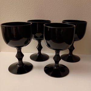 May include: Four black wine glasses with a rounded bowl and a decorative stem. The glasses have a glossy finish and are arranged on a white surface. The stem has a bulbous design, and the base is circular.