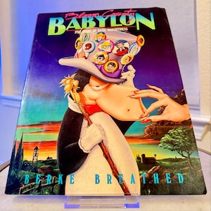 Op de afbeelding: Een vintage boekomslag voor "Bloom County: Babylon" van Berke Breathed. De omslag toont een stripfiguur in smoking en hoge hoed, met een reeks karakterknoppen op de hoed. De titel staat in grote, kleurrijke letters tegen een paars-blauwe achtergrond.