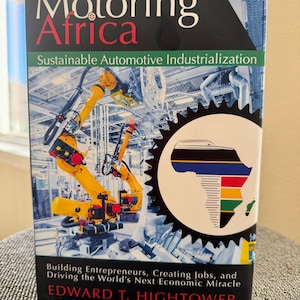 May include: A hardcover book titled "Motoring Africa" with the subtitle "Sustainable Automotive Industrialization." The cover features a photo of yellow robotic arms in a factory setting and a graphic of the African continent.