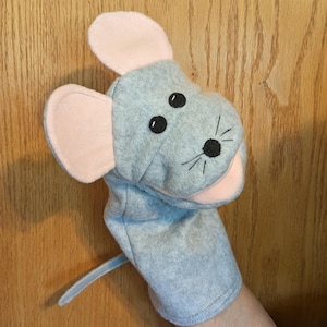 May include: A gray felt mouse hand puppet with pink inner ears. The puppet has black embroidered eyes and whiskers, and a long, thin tail. The puppet is designed to fit over a hand for play.
