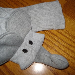 May include: Gray sock puppet with a gray elephant head and black eyes. The puppet is made from a soft, knitted fabric.